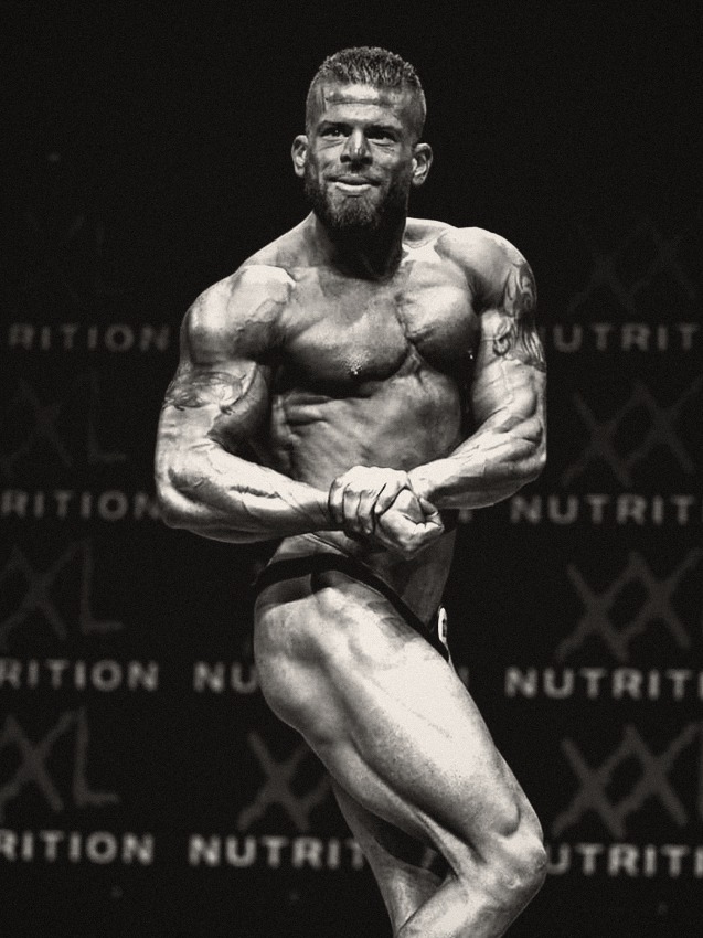 An athlete on stage hitting a side chest pose in contest condition, black-and-white print